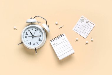 Alarm saati ve bej arkaplandaki kağıt raptiyeli takvim