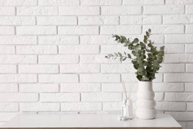 Okaliptüs dalları ve aroma çubukları olan vazo beyaz tuğla duvarın yanındaki odada.