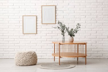 Okaliptüs dallı vazolar, odanın içindeki beyaz tuğla duvarın yanındaki raf ünitesinde.