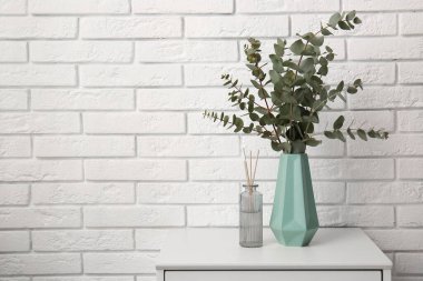 Okaliptüs dalları olan bir vazo beyaz tuğla duvarın yanında, odada.