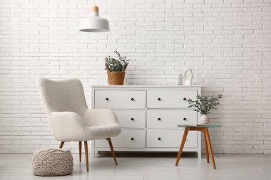 Oturma odasının iç tarafındaki beyaz tuğla duvarın yanındaki çekmecelerin üzerindeki vazoda okaliptüs dalları.