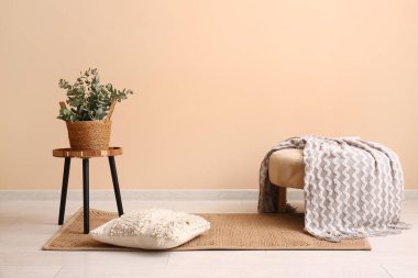 Masada okaliptüs dalları olan hasır sepet ve odada bej duvarın yanında puf.