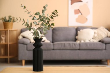 Oturma odasının içindeki masada okaliptüs dalları olan siyah vazo, yakın plan.