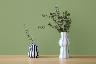 Okaliptüs dalları olan vazolar yeşil duvarın yanındaki masada, yakın plan.