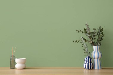 Okaliptüs dalları olan vazolar yeşil duvarın yanındaki odada.