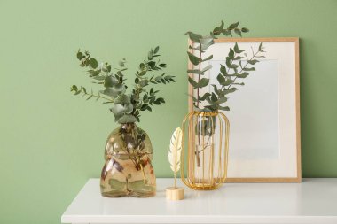 Okaliptüs dallı vazolar, yeşil duvarın yanındaki çekmecelerin üzerinde, yakın plan.