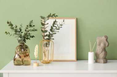 Okaliptüs dallı vazolar yeşil duvarın yanındaki çekmecelerin üzerinde.