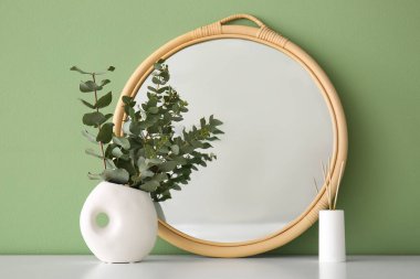 Okaliptüs dallı vazo ve yeşil duvarın yanındaki masada ayna, yakın plan.