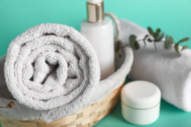 Hasır sepetli kompozisyon, temiz yumuşak havlular, turkuaz arka planda şişe ve bir kavanoz kozmetik ürünü, yakın plan