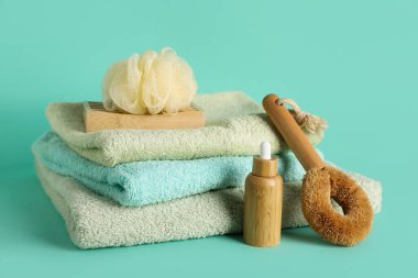 Turkuaz arka planda bir yığın temiz havlu, banyo süngeri ve bir şişe kozmetik ürünü, yakın plan.