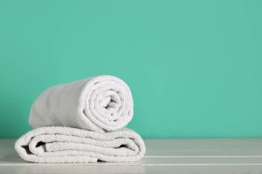 Turkuaz duvarın yanındaki beyaz masada temiz yumuşak havlular, yakın plan.
