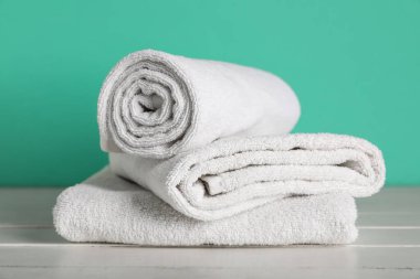 Turkuaz duvarın yanındaki beyaz masada temiz yumuşak havlular, yakın plan.