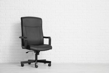 Beyaz tuğla duvarın yanındaki ofis siyah koltuğu.