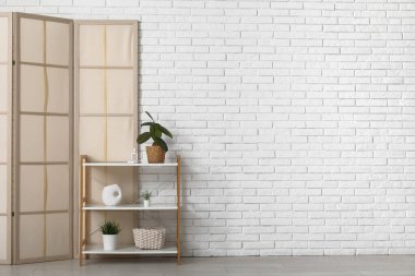 Beyaz tuğla duvarın yanında katlanan ekran ve raf ünitesi.