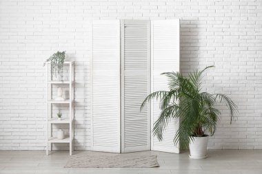 Katlanan ekran, raflama ünitesi ve beyaz tuğla duvarın yanındaki ev bitkisi.