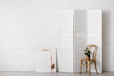 Katlanan ekran, resimler ve beyaz tuğla duvarın yanındaki ev bitkisi.