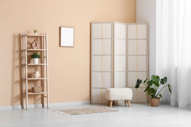 Katlanan ekran, pouf ve çiçek bej duvarın yanında.