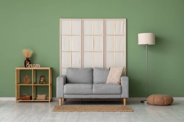 Katlanan ekran, kanepe ve zemin lambası oturma odasının içindeki yeşil duvarın yanında.