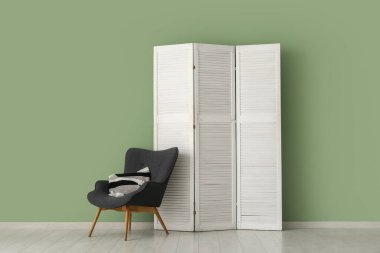 Katlanan ekran ve sandalye yeşil duvarın yanında.