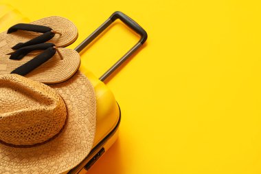 Çanta, şapka ve parmak arası terlikler sarı arka planda, yakın plan.