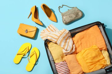 Mavi arka planda giysiler ve aksesuarlarla dolu bavul, yakın plan.