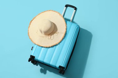 Mavi arka planda bavul ve hasır şapka