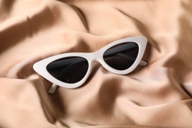 Arka plan olarak bej ipek kumaş üzerinde güneş gözlüğü, yakın plan