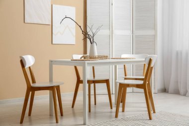 Yemek odasının içinde masa ve bej duvarın yanında sandalyeler.