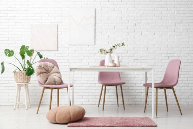 Beyaz tuğla duvarın yanında puf, masa ve sandalyeli yemek odasının içi.