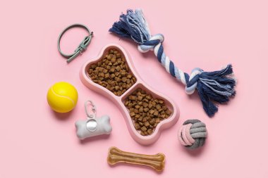 Kuru hayvan mamasıyla kemik şeklinde kase ve pembe arka planda aksesuarlar.