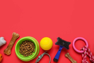 Kırmızı arka planda kuru hayvan maması ve aksesuarları olan bir kase.