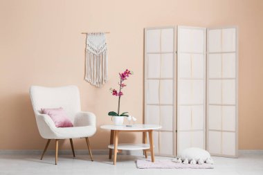 Kahve masası, koltuk ve katlanan ekran odanın içindeki bej duvarın yanında.