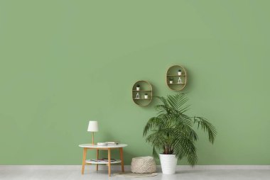 Çiçek, masa ve pouf, odanın içindeki yeşil duvarın yanında.