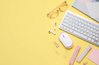 Klavye, fare, kulaklık ve sarı arka planda kırtasiye malzemesi ile kompozisyon