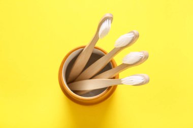 Sarı arka planda ahşap diş fırçaları olan cam, yakın plan.