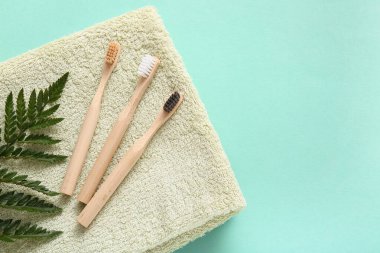 Tahta diş fırçaları, havlu ve turkuaz arka planda yeşil yaprak, yakın plan.