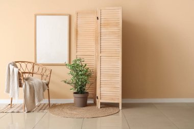 Ahşap katlanır ekran, hasır koltuk ve bej duvarın yanındaki ev bitkisi.