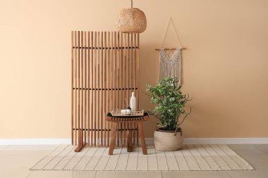 Odanın içinde bej duvarın yanındaki ahşap katlı ekran, masa ve çiçek.