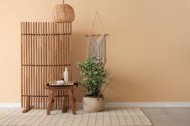 Odanın içinde bej duvarın yanındaki ahşap katlı ekran, masa ve çiçek.