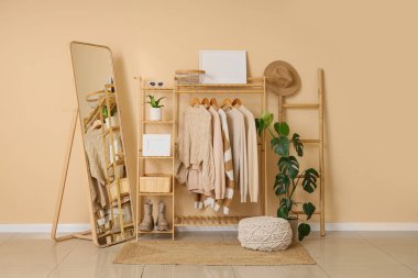 Döşeme aynası, ahşap askı, şık kıyafetler ve bej duvarın yanında aksesuarlar, odanın içinde.