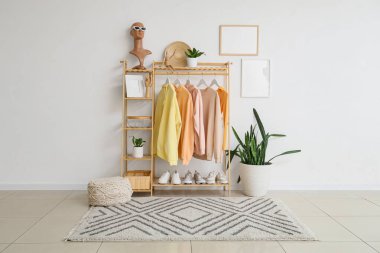 Odanın içinde beyaz duvarın yanında şık kıyafetler, ayakkabılar ve ev bitkileriyle ahşap askı.