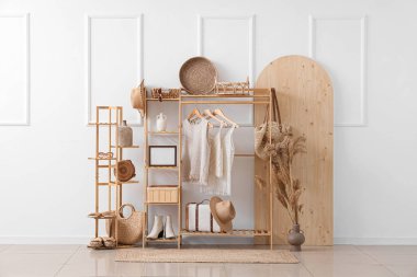 Odanın içinde beyaz duvarın yanında şık giysileri olan ahşap raf ve raf ünitesi.