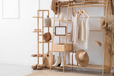 Odanın içinde beyaz duvarın yanında şık giysileri olan ahşap raf ve raf ünitesi.