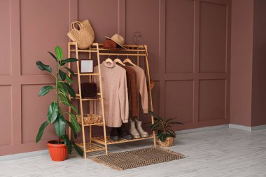 Odanın içindeki kahverengi duvarın yanında şık kıyafetler ve aksesuarlarla ahşap askı.