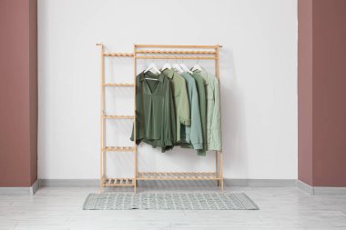 Odanın iç tarafındaki beyaz duvarın yanında şık giysileri olan ahşap askı.