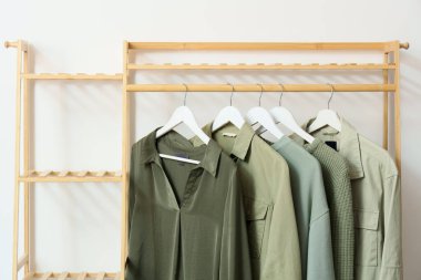 Odasında beyaz duvarın yanında şık kıyafetler olan ahşap askı, yakın plan.