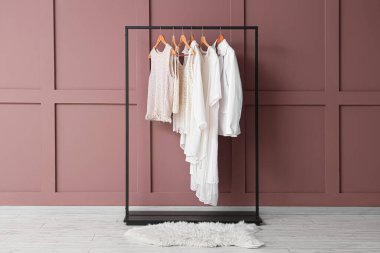 Odanın iç tarafındaki kahverengi duvarın yanında şık kıyafetler var.