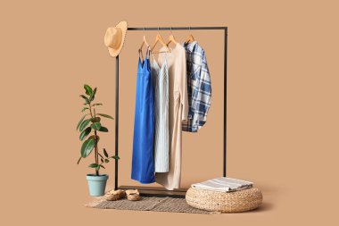 Siyah askılık, şık kıyafetler ve bej arka planda ayakkabılar.