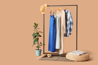 Siyah askılık, şık kıyafetler ve bej arka planda ayakkabılar.