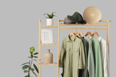 Gri arka planda şık kıyafetler ve aksesuarlarla ahşap askı, yakın plan.